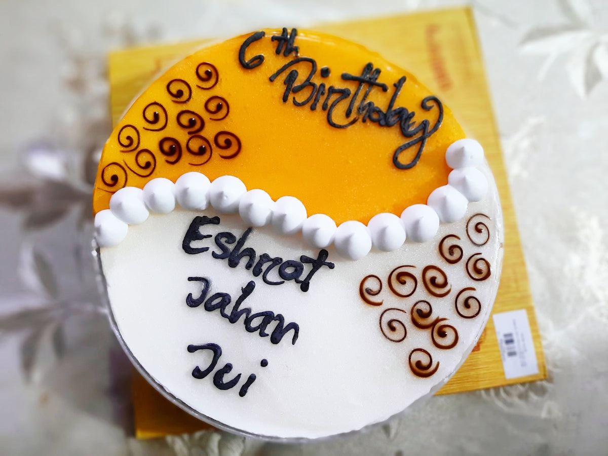 6歳の誕生日ケーキ。オレンジとホワイトのツートンデザインに「Eshrat Jahan Jui」と手書き風文字。チョコ渦巻きとパールデコレーションが可愛らしく仕上げ。