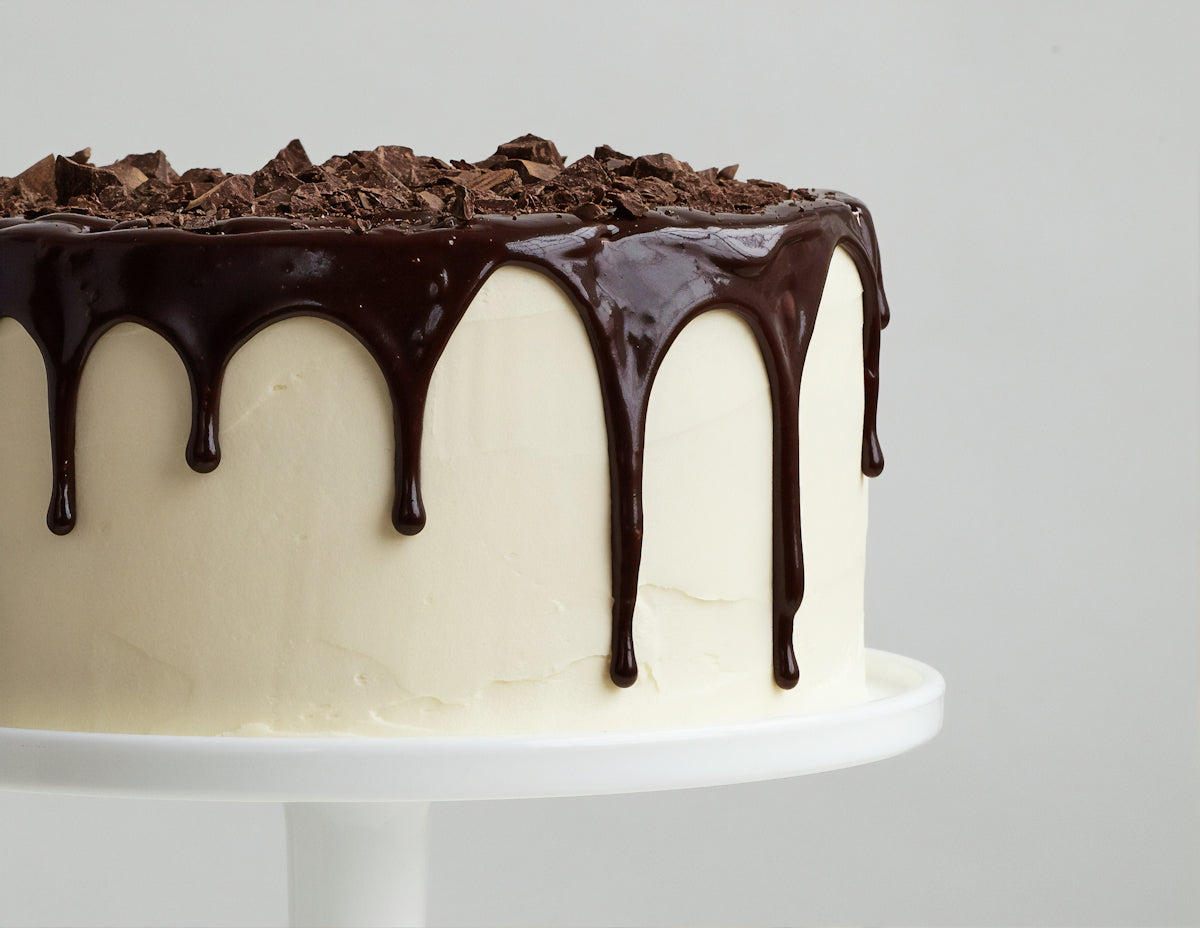 白い陶器の皿にのった、チョコレートシロップのかかった白いケーキ